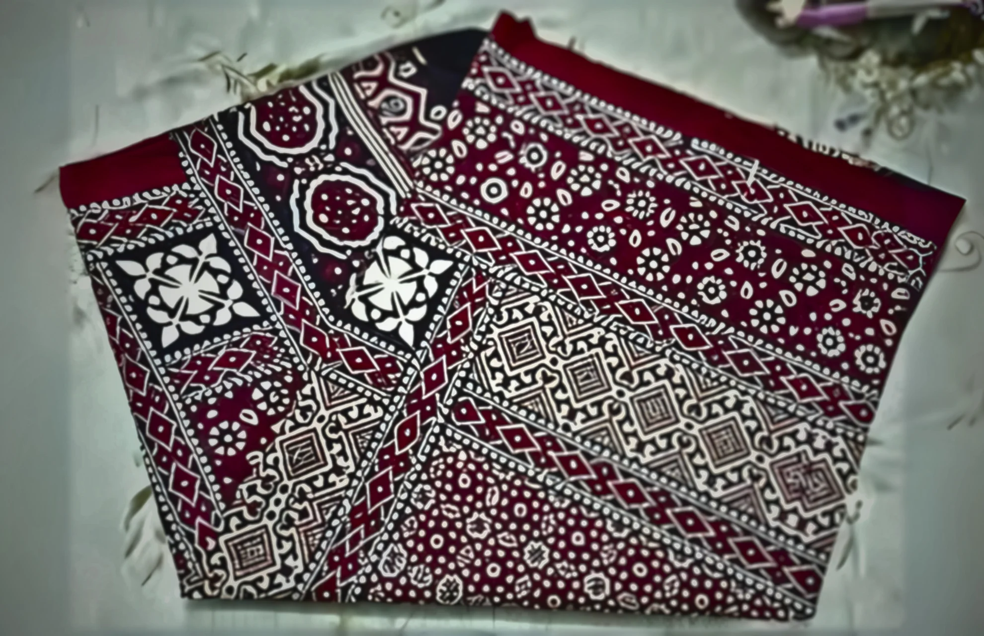A red and black patterned scarf elegantly draped on a neatly made bed, showcasing its vibrant colors and intricate design.