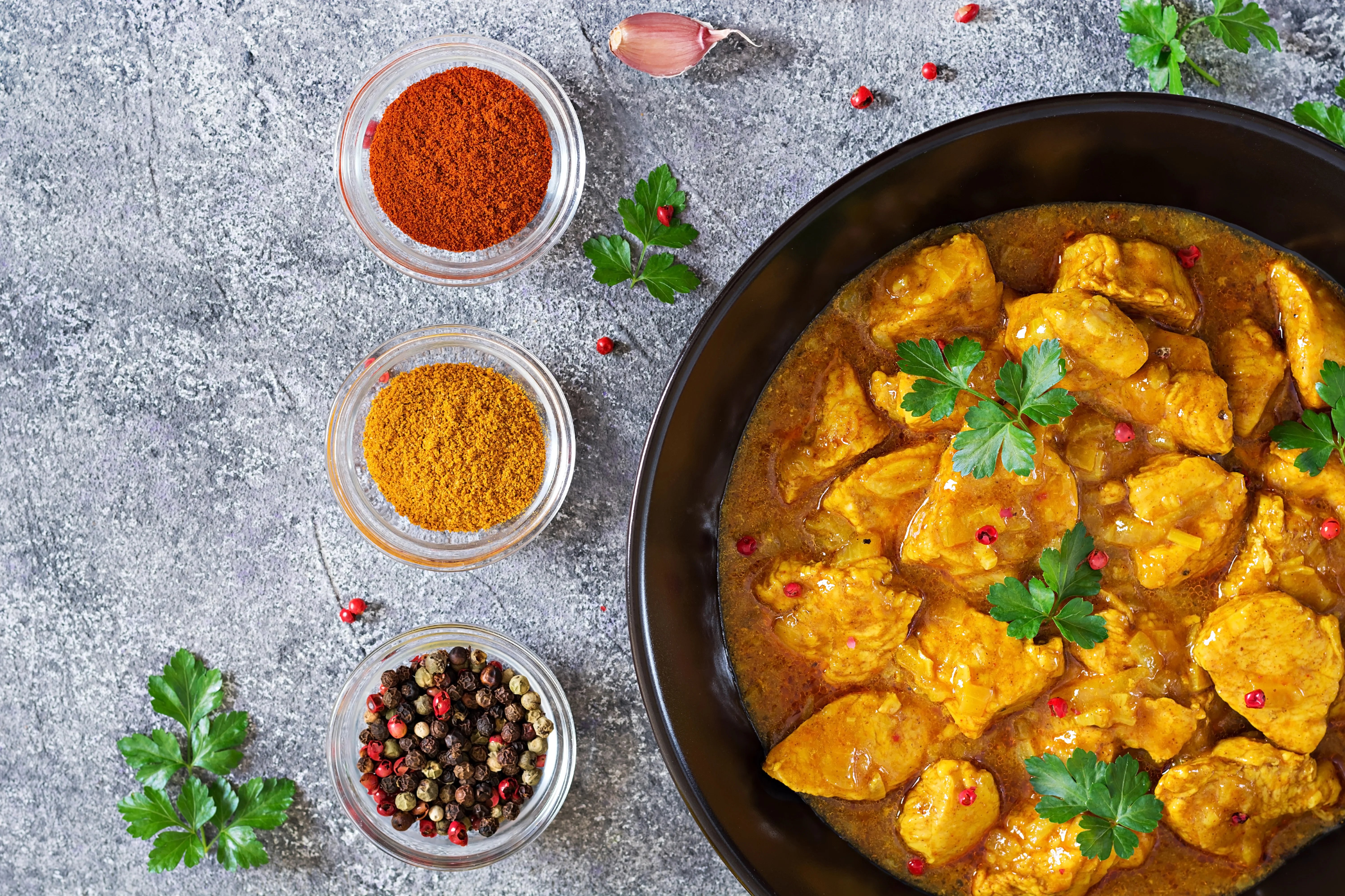 A vibrant bowl of chicken curry garnished with fresh herbs and an array of colorful spices, showcasing rich flavors.