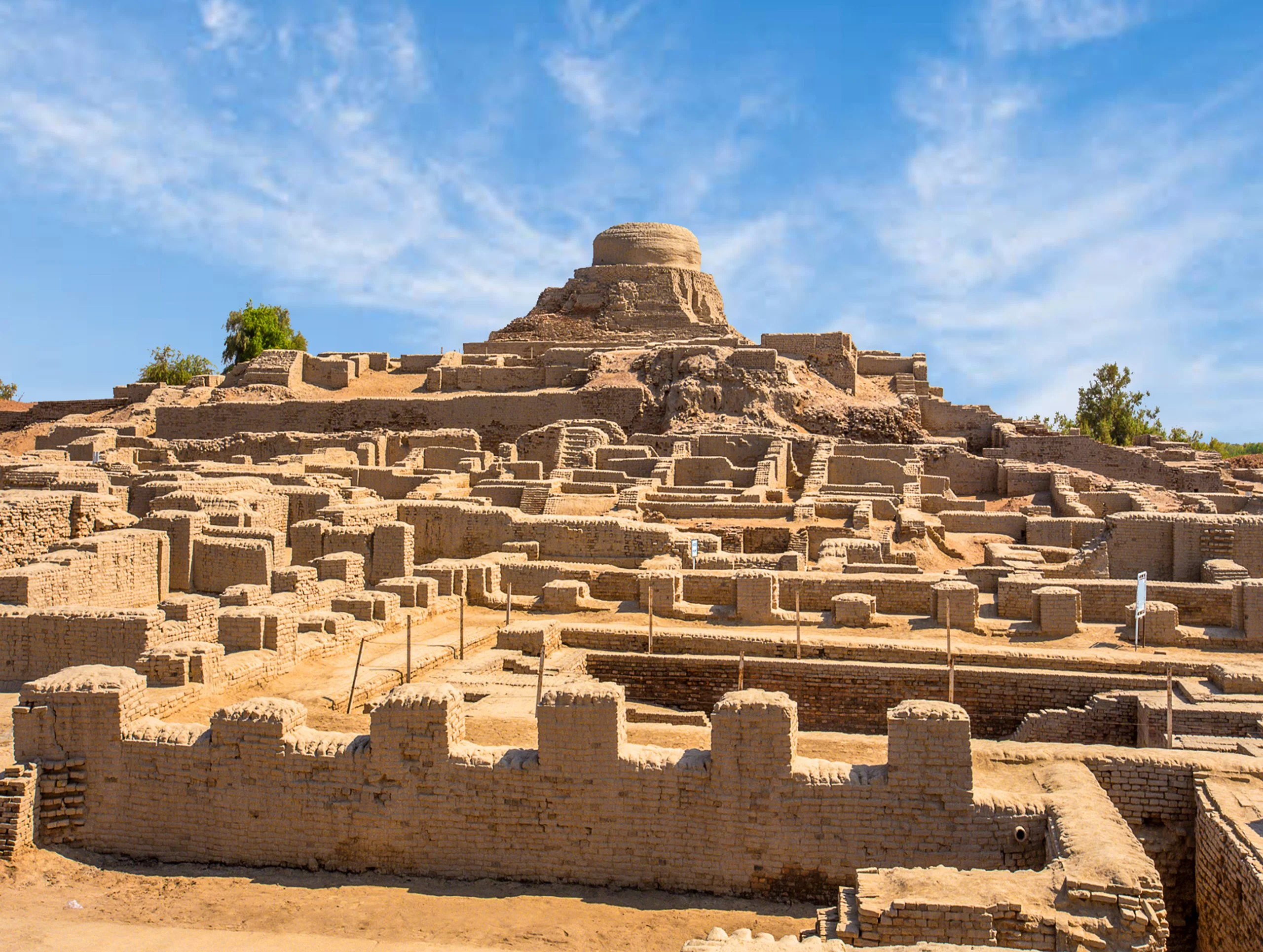 Ancient city ruins emerge from the desert landscape, showcasing weathered stone structures against a clear blue sky.